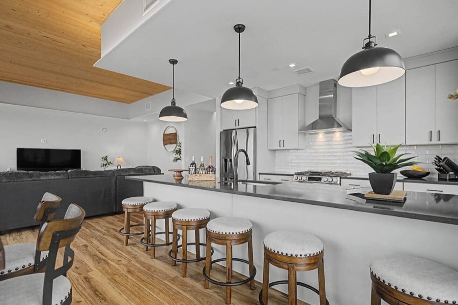 One of the penthouse's two kitchens — five round stools along the dark quartz island, black pendants, and the den's sectional beyond