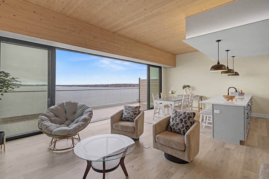Living area of Residence 602 with swivel armchairs and a glass coffee table facing wall-to-wall windows over Muskegon Lake