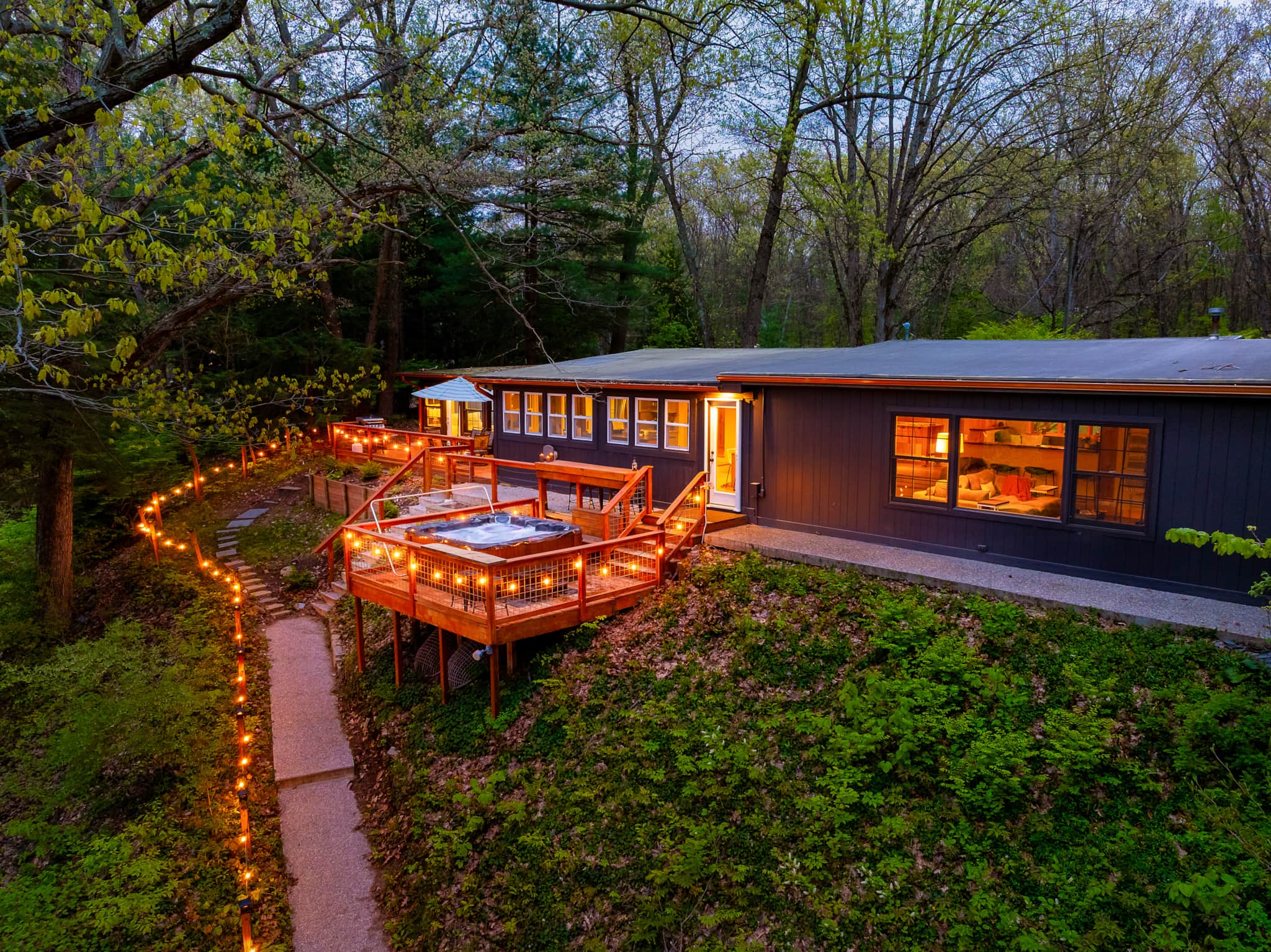 Fire & Water's dark-sided cabin at dusk in Fennville, string lights tracing the path down to the hot-tub deck above the Kalamazoo River bank