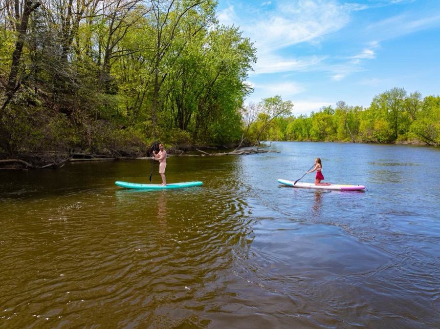 Two guests paddleboarding the calm, tree-lined Kalamazoo River right off the property's dock