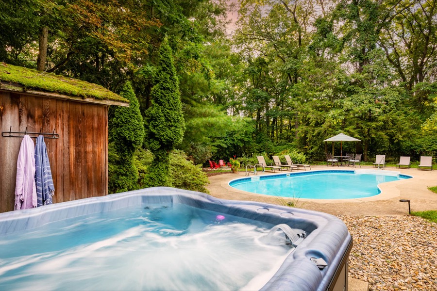 Backyard hot tub in the foreground with a sparkling inground pool and lounge chairs beyond, in Grand Beach