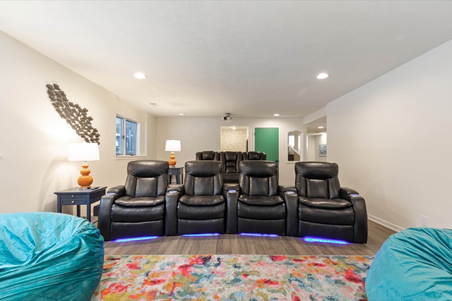 The theater room: two rows of black leather recliners with glowing base lights, bean bags up front, and the projector overhead