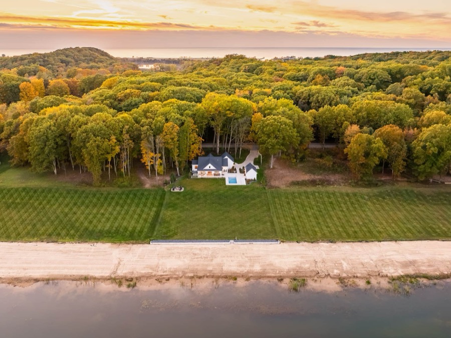 Aerial sunset view: the white farmhouse and pool in a clearing of autumn forest, the private lake in front and Lake Michigan on the horizon